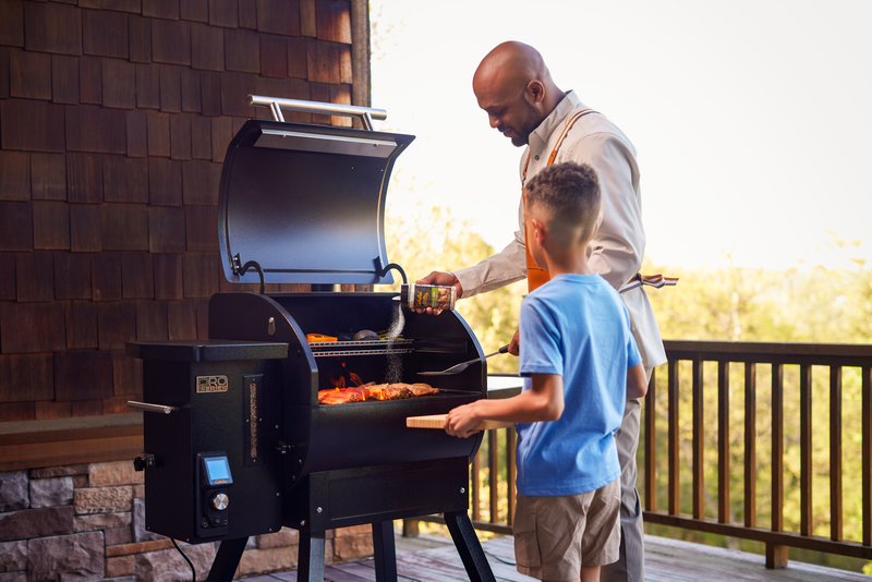 Father and son cooking on a Pro Series pellet grill on the deck, preparing a summer meal with BBQ gear from Bass Pro Shops.