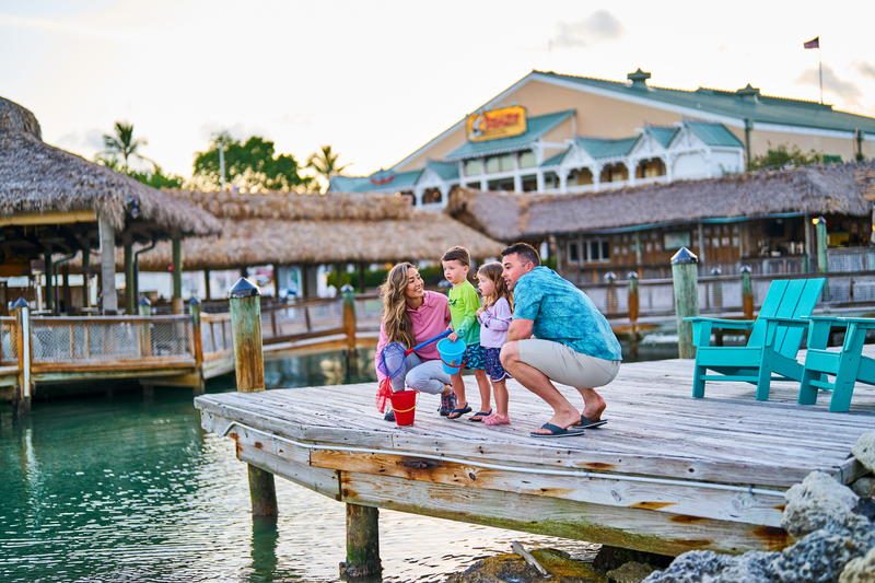 Family enjoying waterfront fun on the dock at Bass Pro Shops, with two young kids exploring the water using nets and a bucket during a sunny day at the marina.